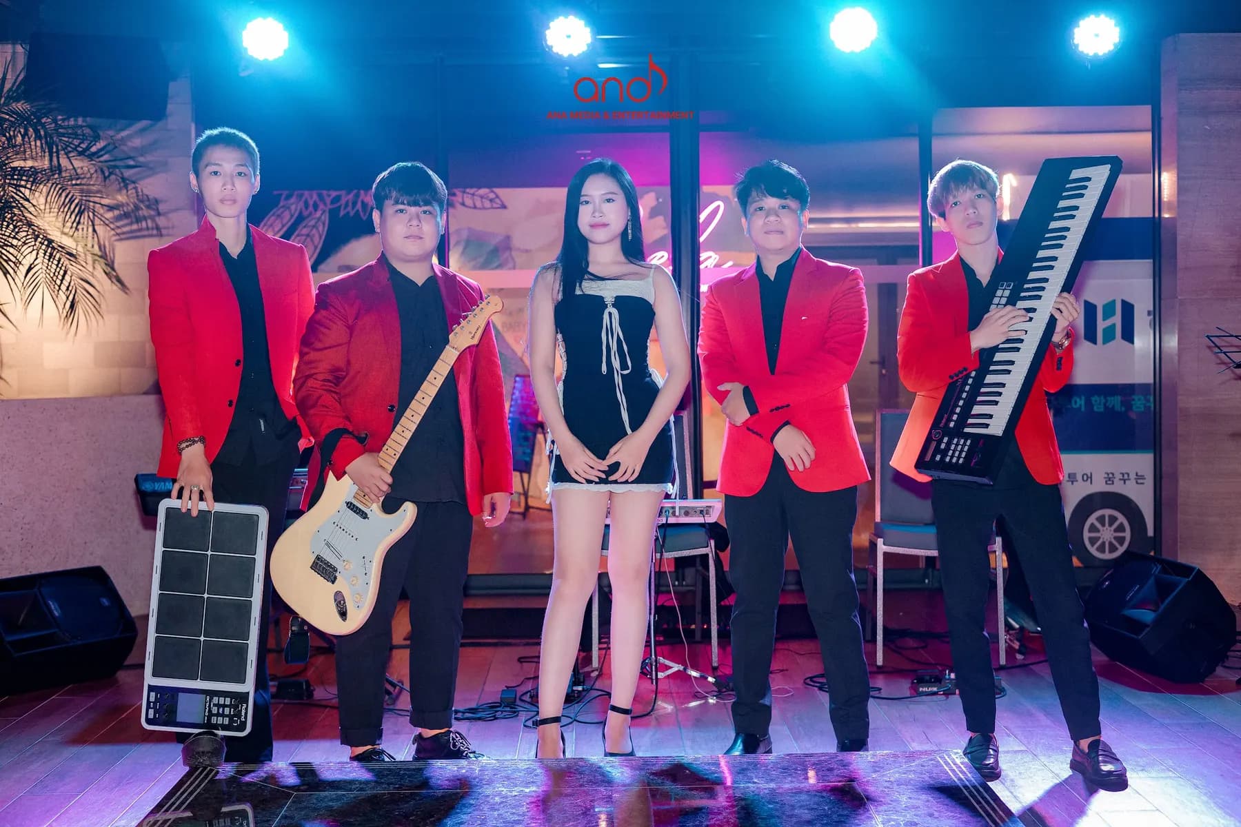 Five band members in red jackets on a lit stage