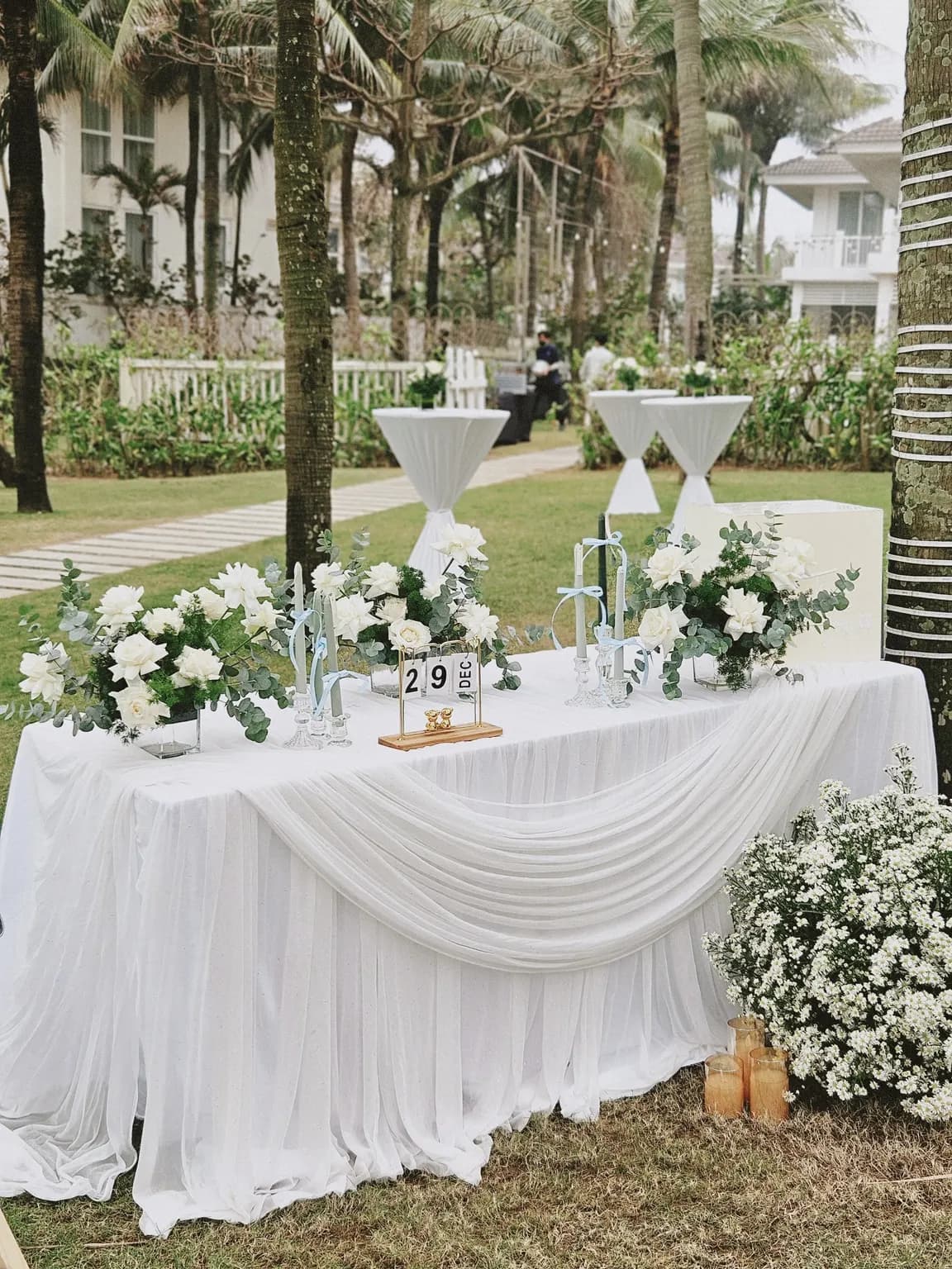 Welcome table draped in white under palm trees