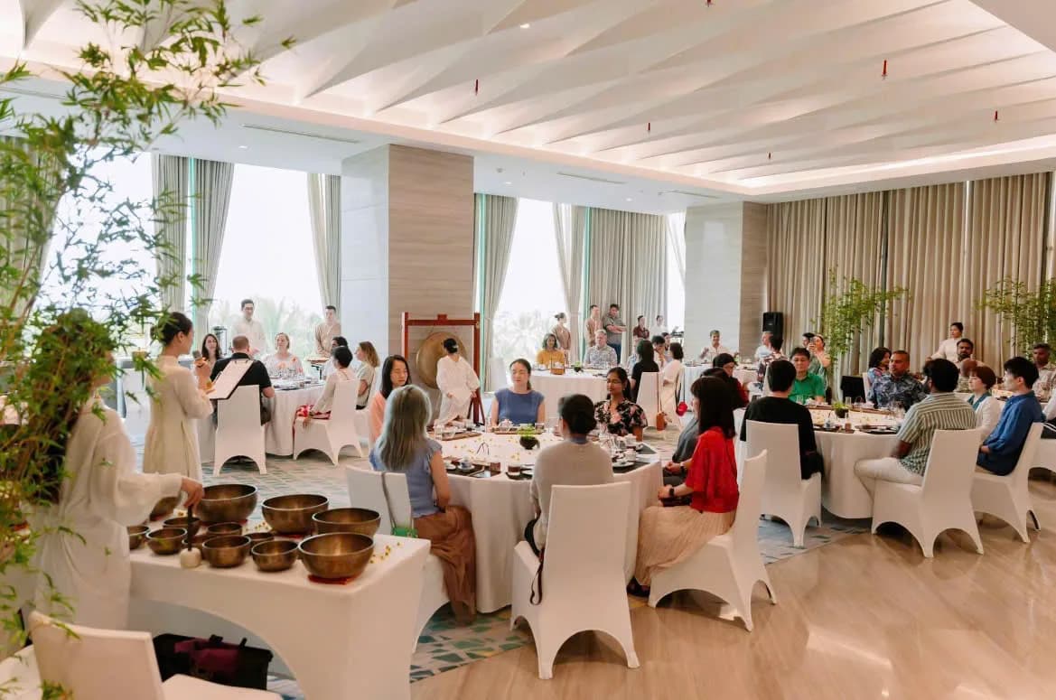 Singing bowl sound bath for conference guests seated at round tables in a bright hotel ballroom