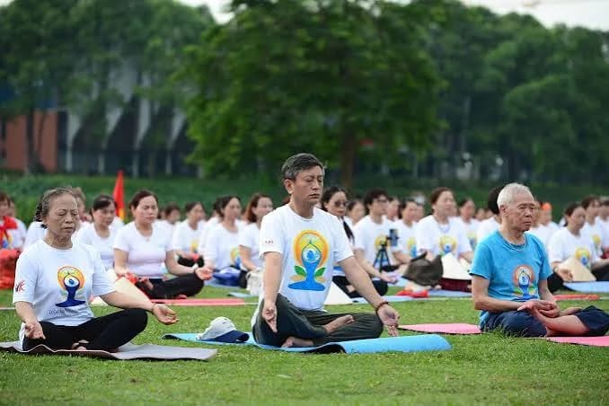 Large group in matching T-shirts meditating cross-legged on mats in a park