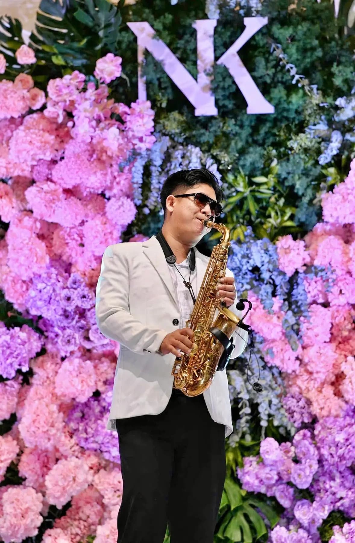 Saxophonist in a white suit in front of a floral backdrop