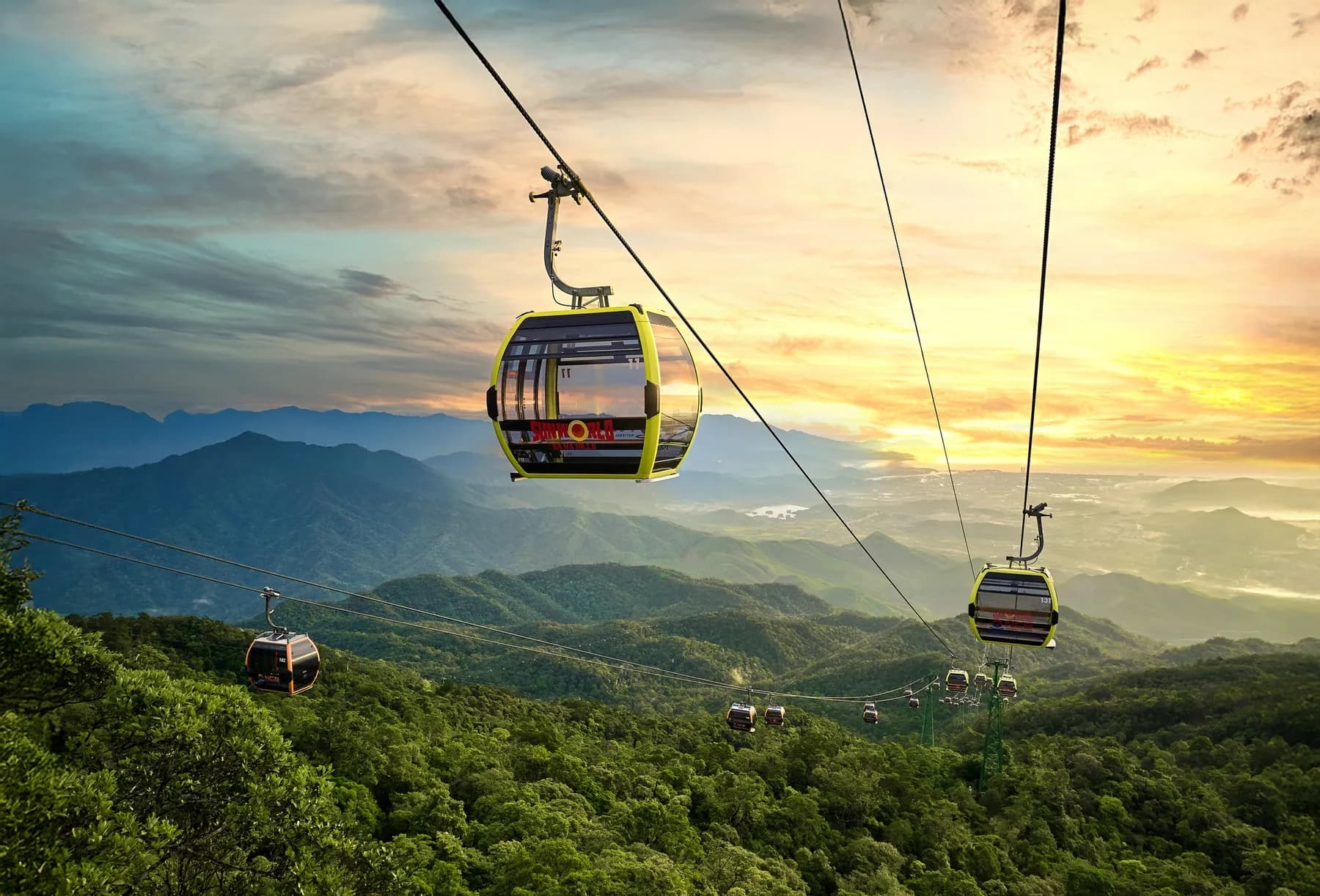 Cable cars rising over forested mountains to Ba Na Hills at sunset