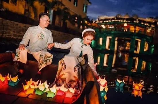 Couple in ao dai on a boat among floating flower lanterns on the Hoai river at night