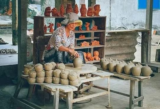 Potter shaping clay among finished jars in Thanh Ha pottery village