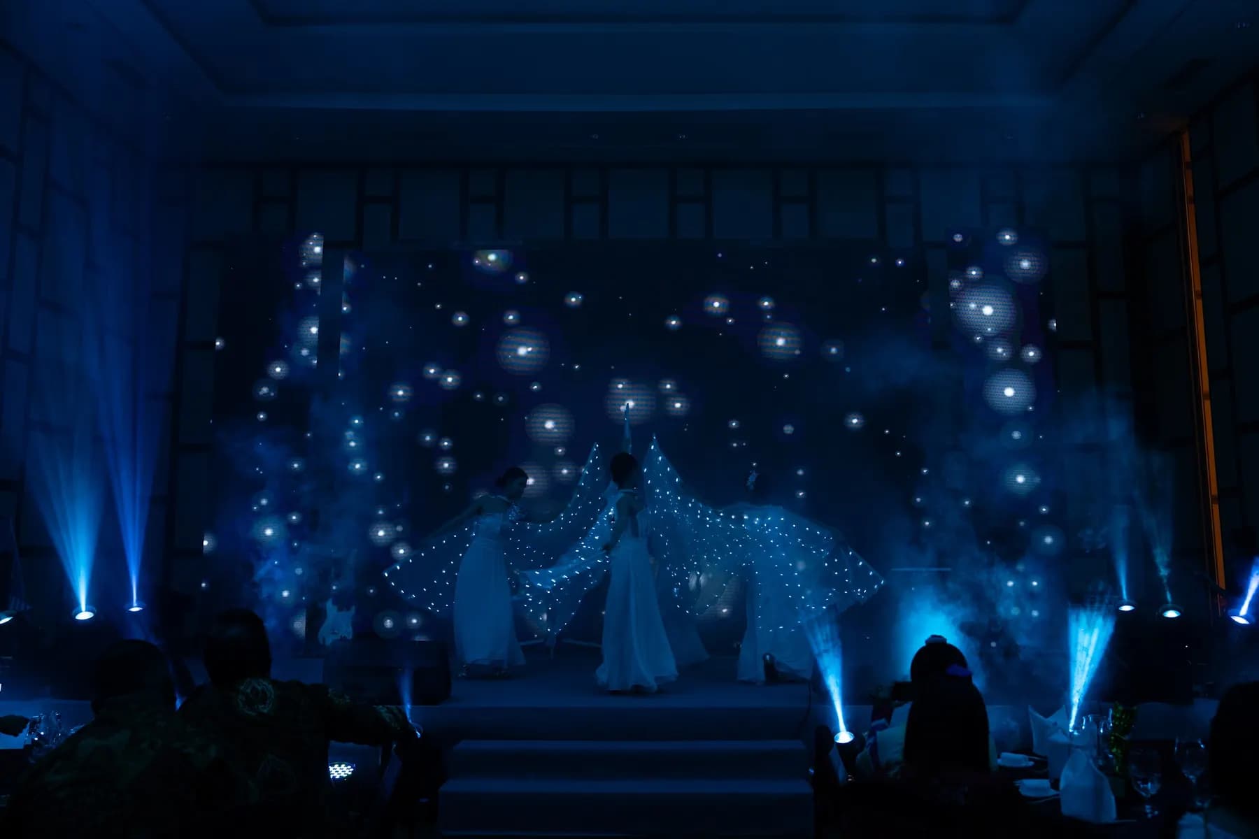 LED wing dance on a darkened stage under blue beams
