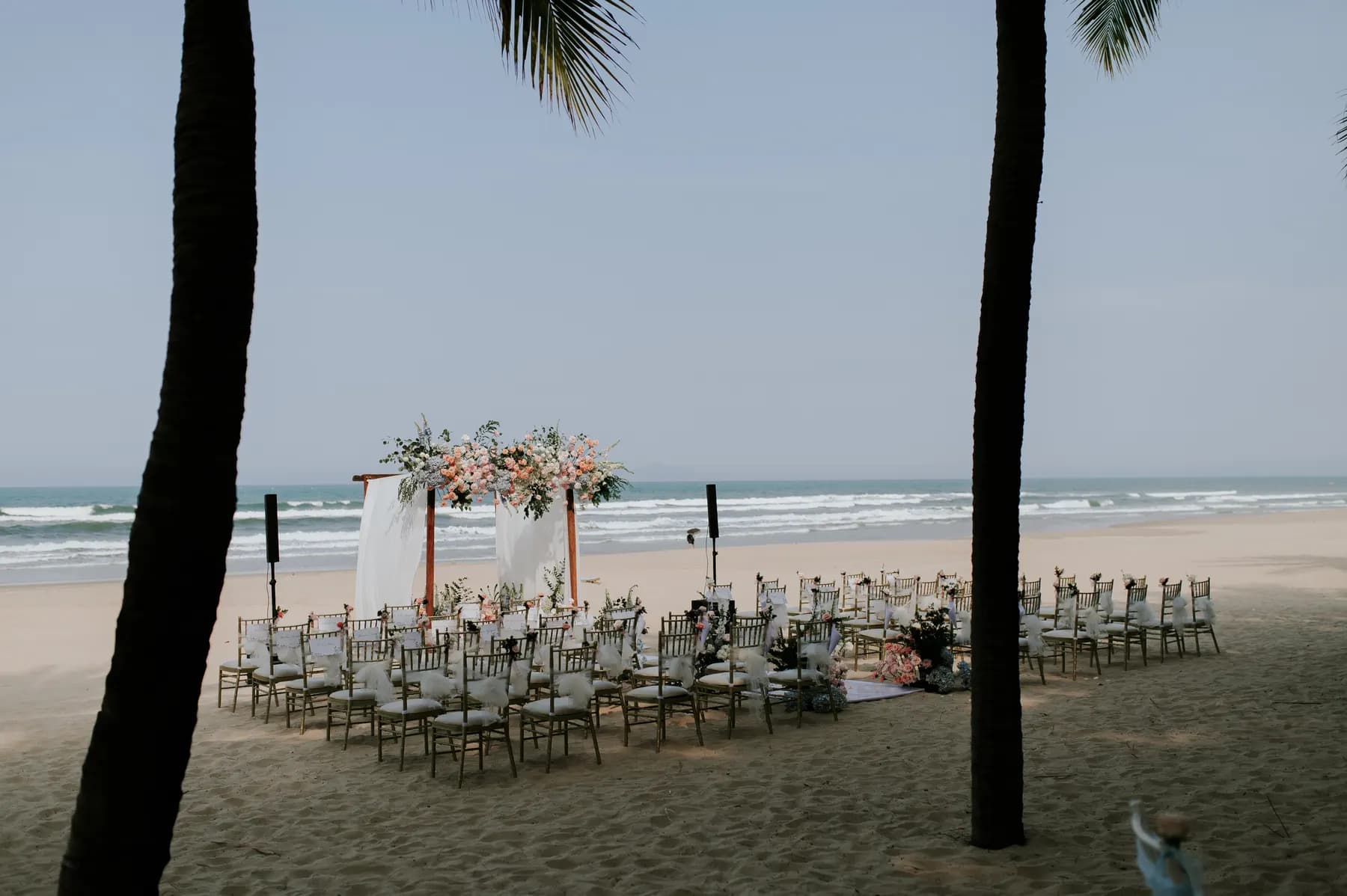 Beach wedding setup framed by palm trees